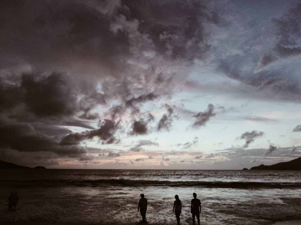 grayscale photo of three person walking on seashore during sunset preview