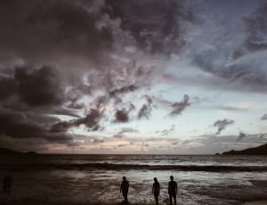 grayscale photo of three person walking on seashore during sunset thumbnail