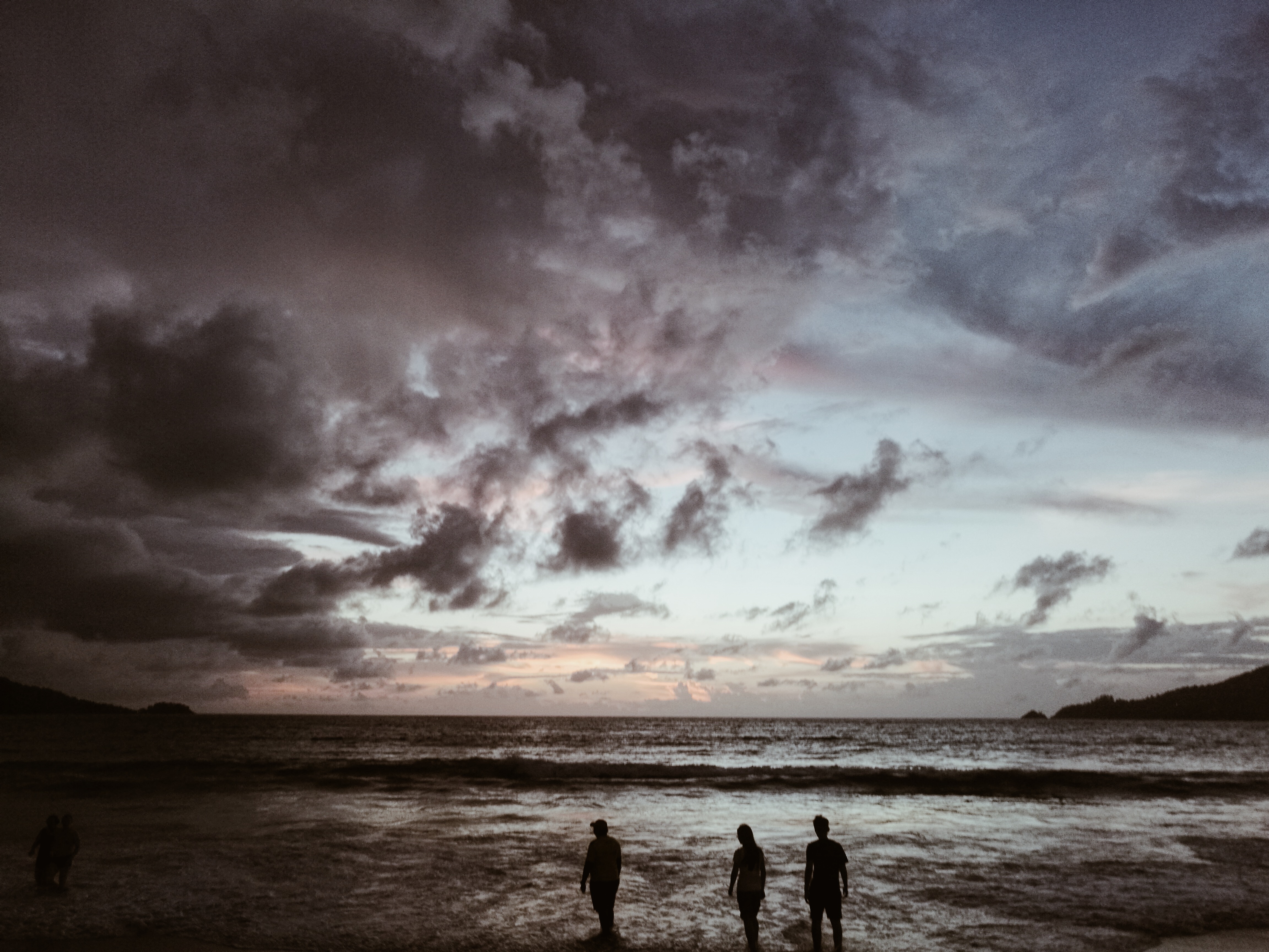 grayscale photo of three person walking on seashore during sunset
