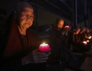 monks holding candles  while sitting down in a line thumbnail