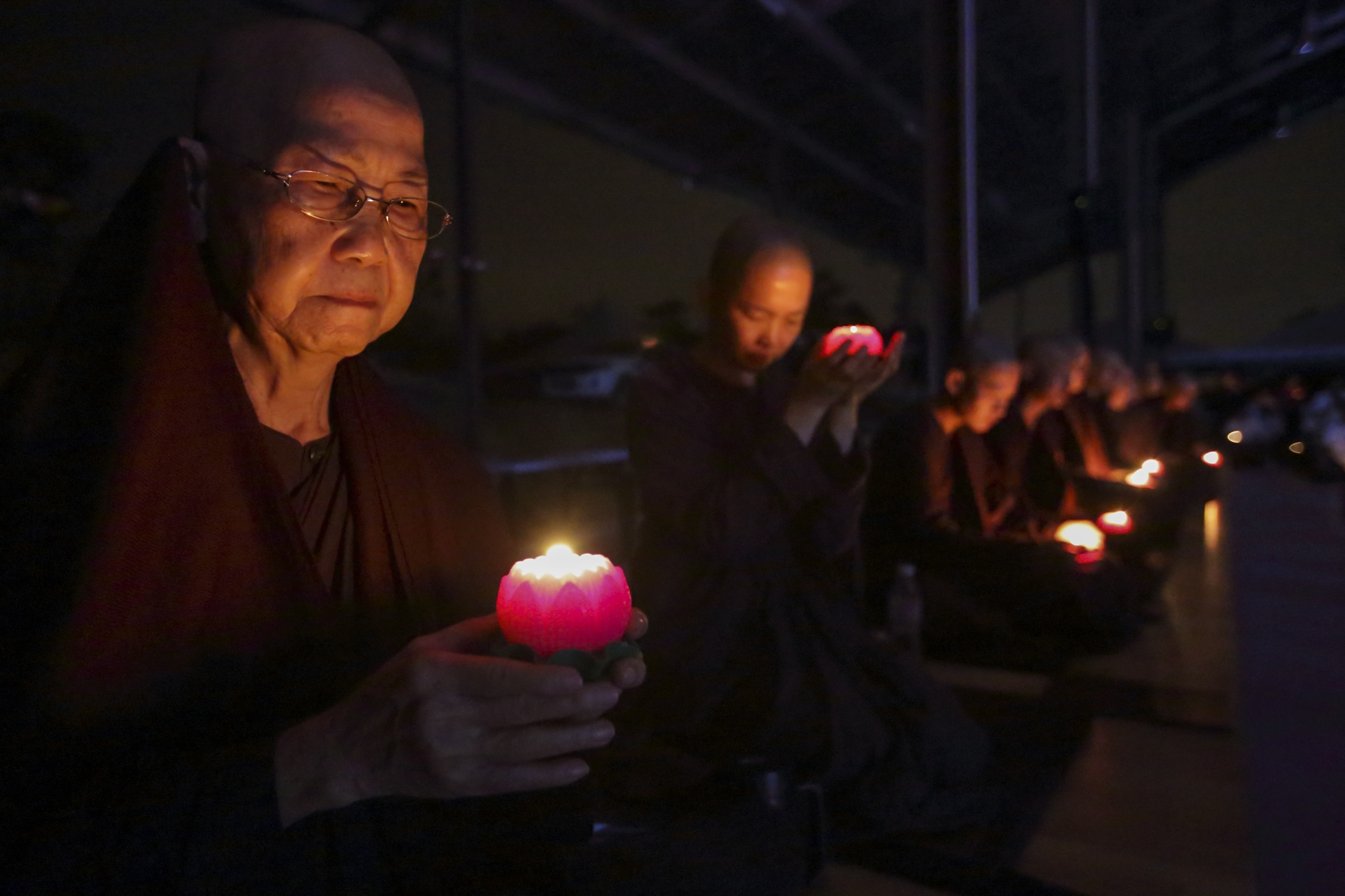 monks holding candles  while sitting down in a line