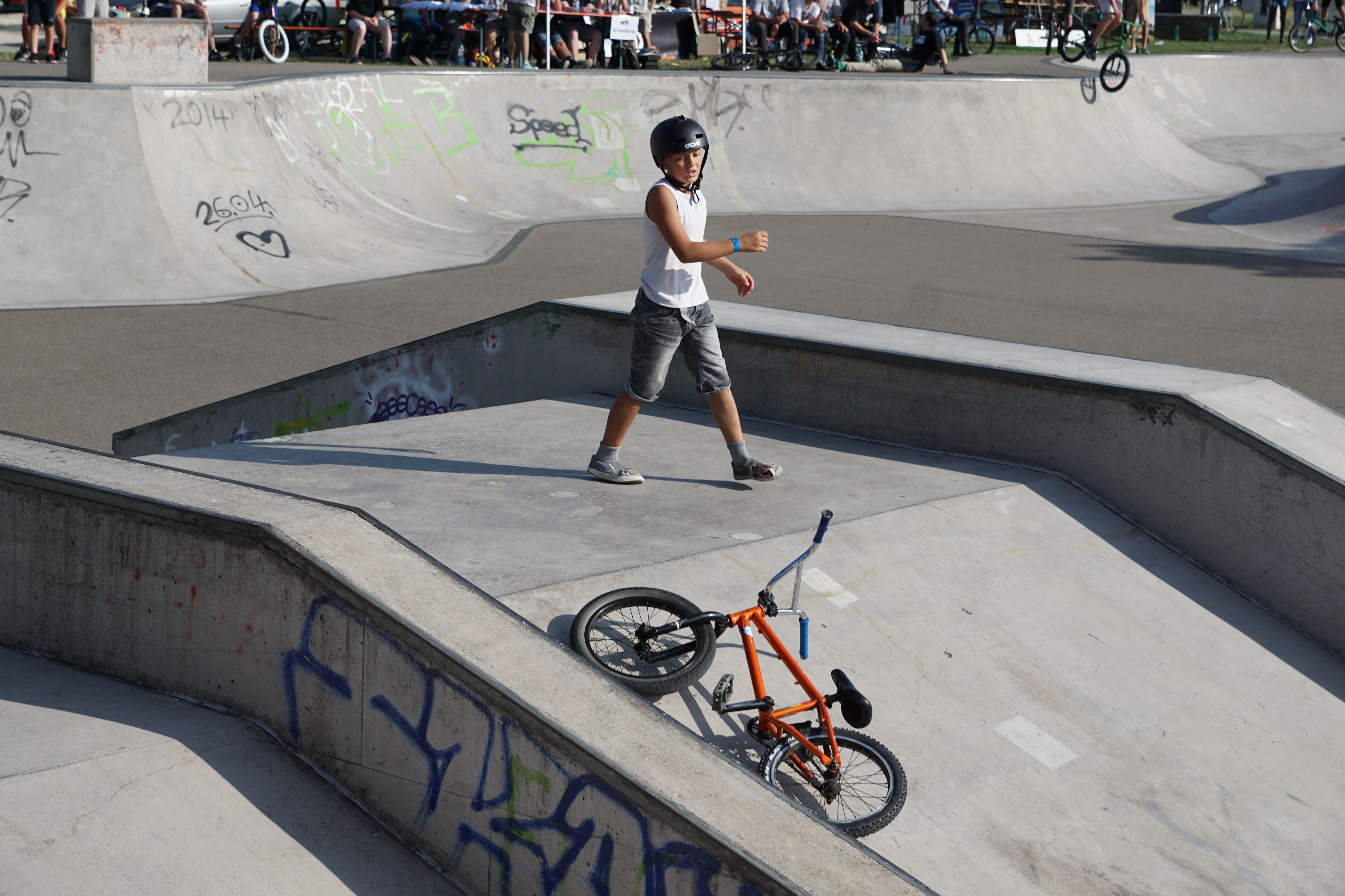 man wearing helmet standing on the middle of ramp his bmx bike on the ground