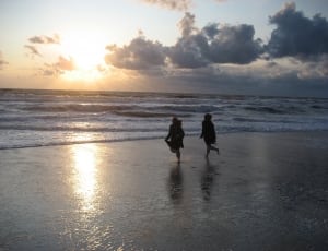 silhouette of two person running on beach during daytime thumbnail