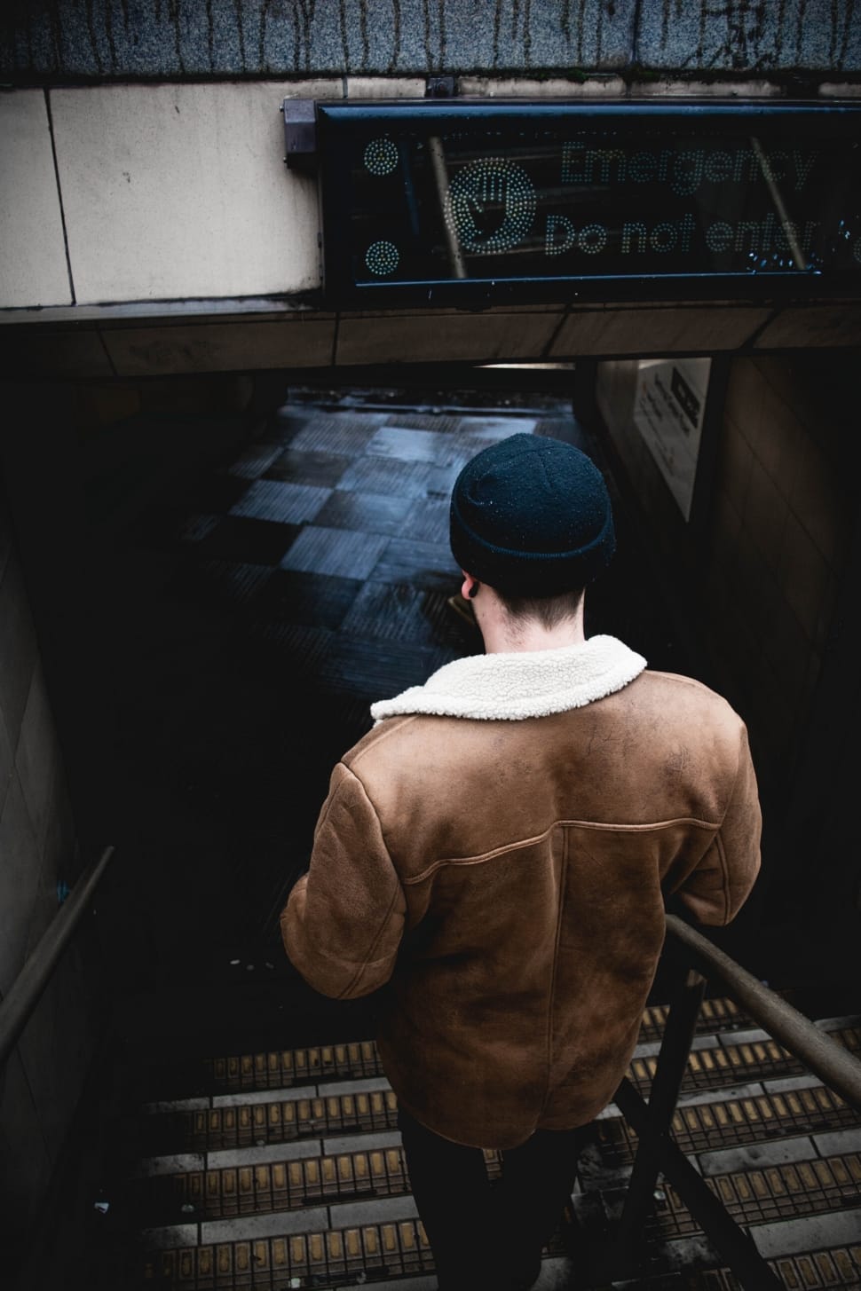 man in brown jacket with black knit cap taking staircase preview