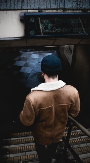 man in brown jacket with black knit cap taking staircase thumbnail