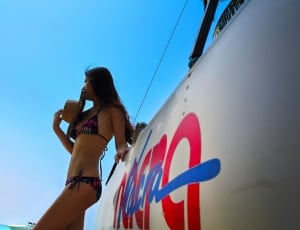 woman wearing bikini set holding sun hat leaning on white surface under blue sky thumbnail