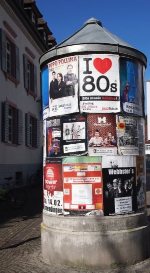 gray concrete structure covered with assorted posters near city buildings during daytime thumbnail