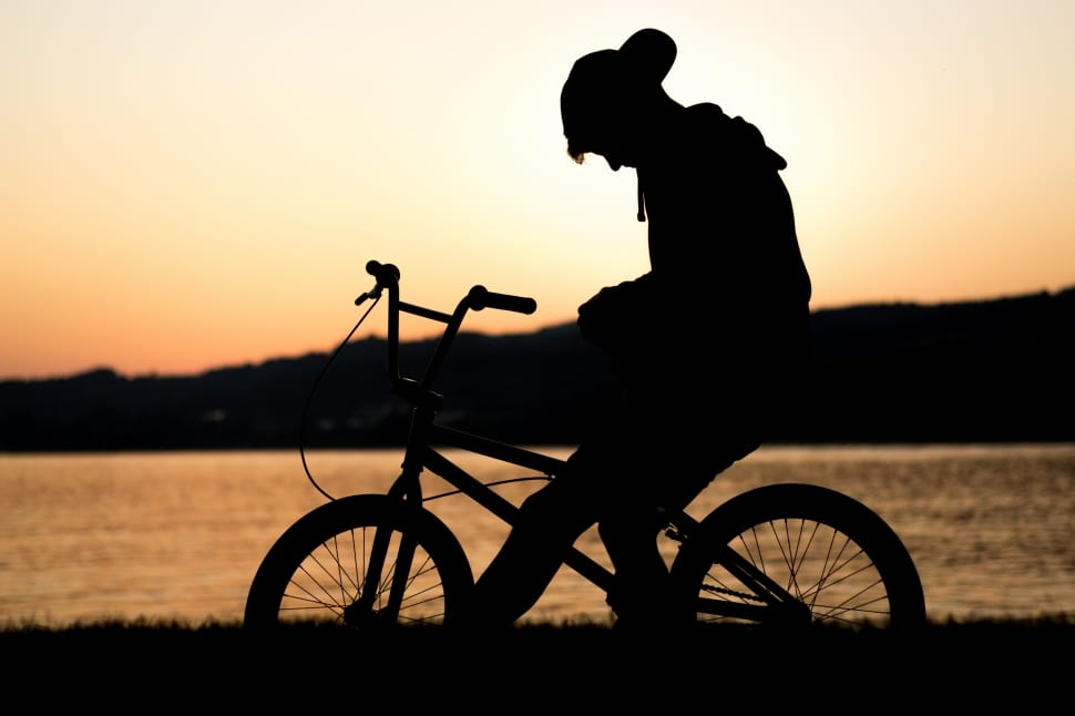 silhouette of man riding bike beside calm sea preview