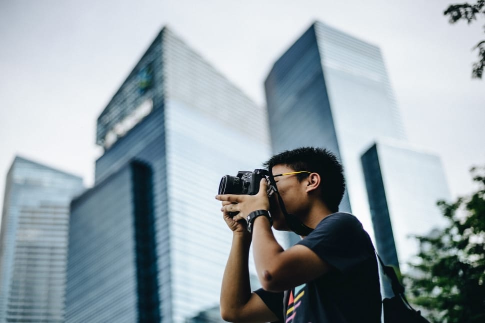 man in black shirt taking photo using black dslr near high rise building at daytime preview