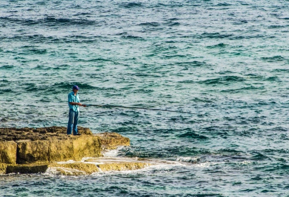 man in blue button-up shirt fishing on the ocean preview