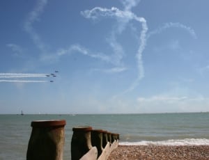 five jetplane with contrails performing near body of water during daytime thumbnail