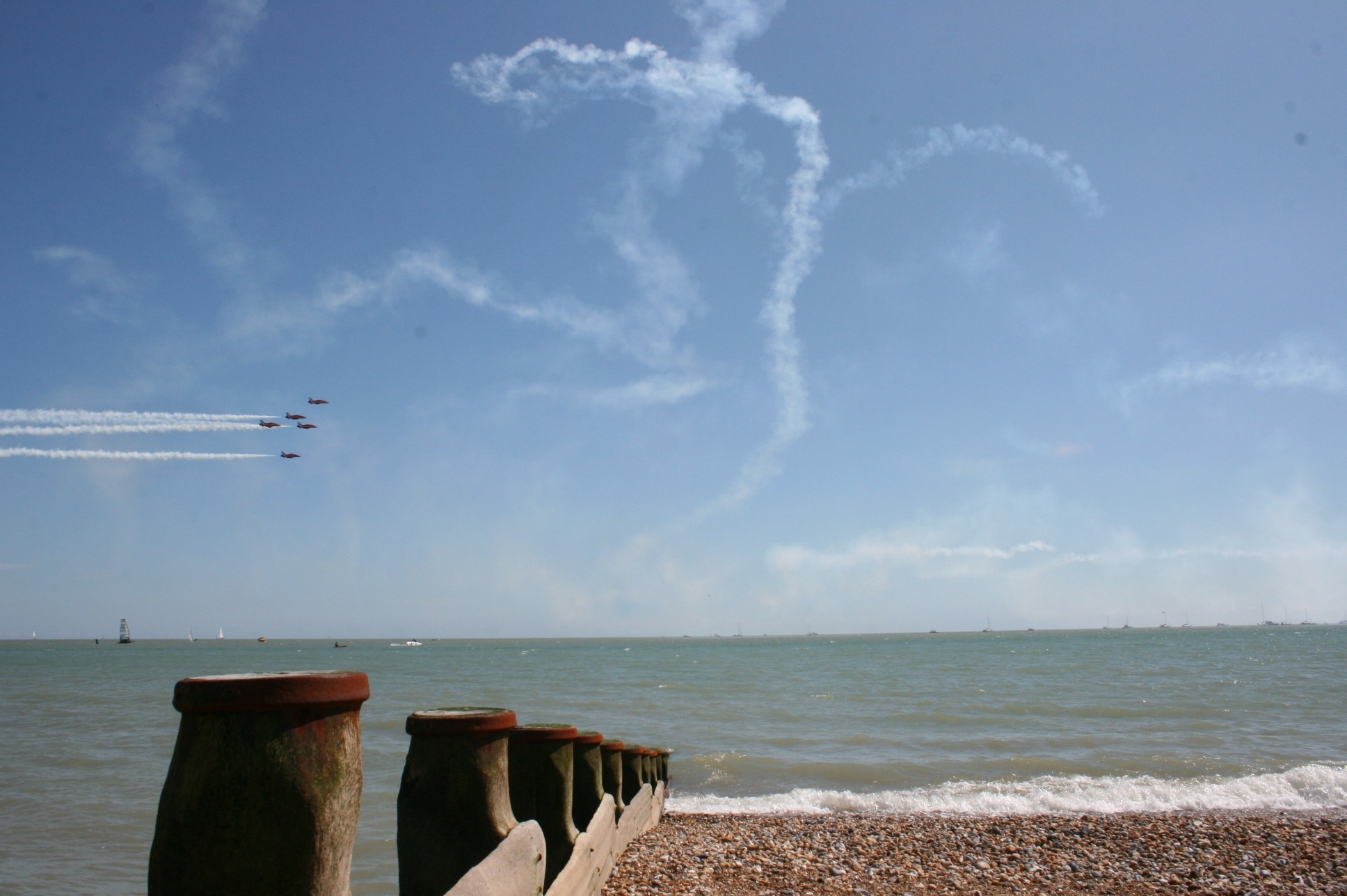 five jetplane with contrails performing near body of water during daytime