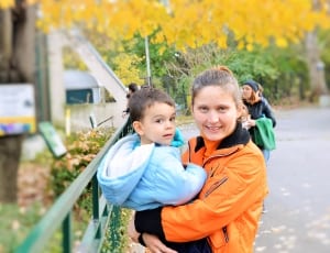 woman carrying his child in teal full zipped jacket thumbnail