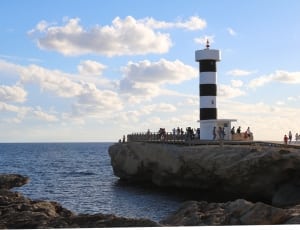 people near white and black concrete lighthouse near blue sea under blue and white cloudy sky during daytime thumbnail