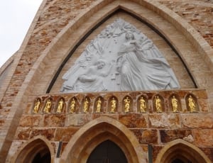 low angle photo of man kneeling near a woman in dress statue on concrete building thumbnail