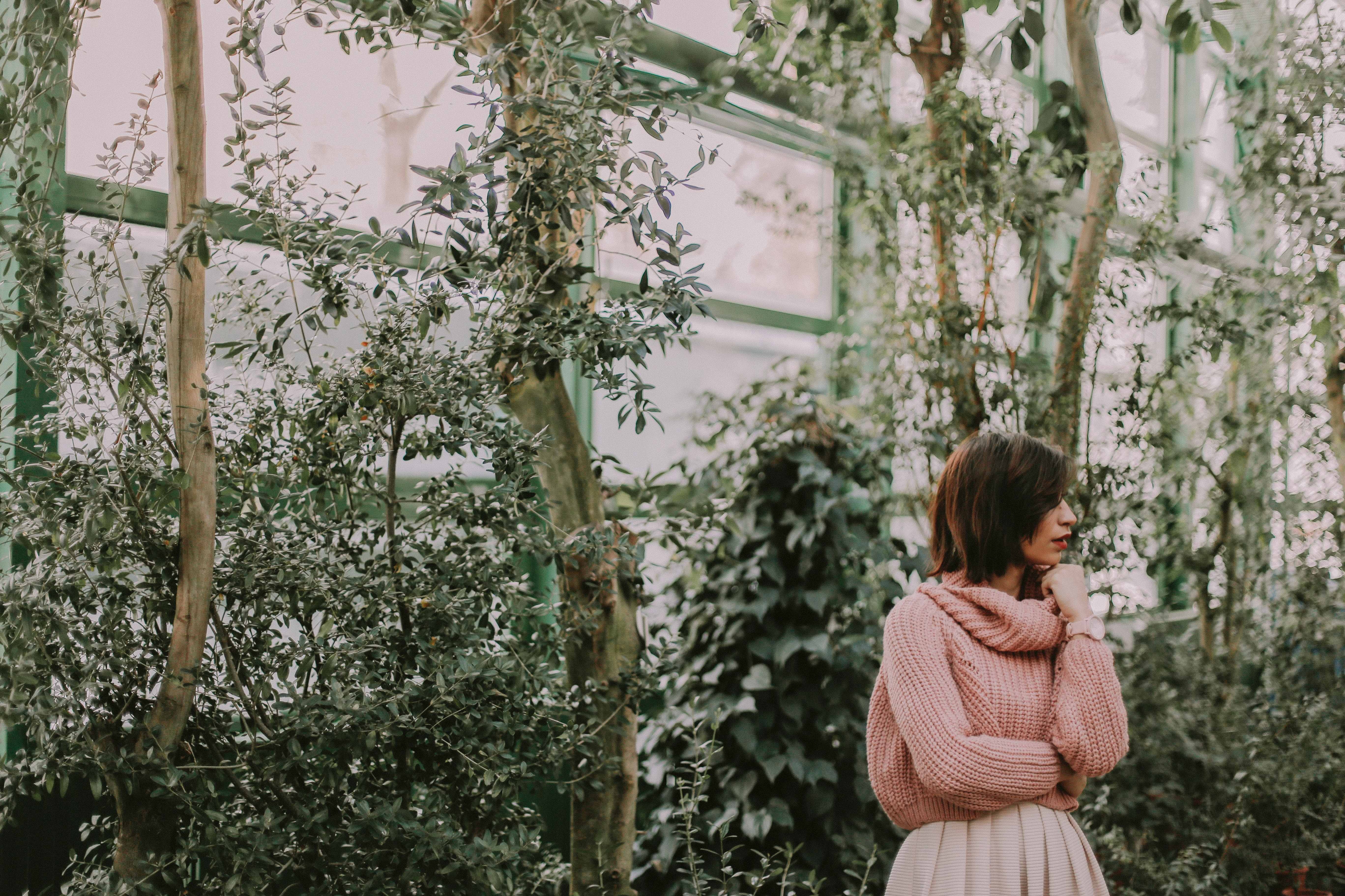 woman wearing pink knitted sweater and pink skirt at the back theres a green hanging plants