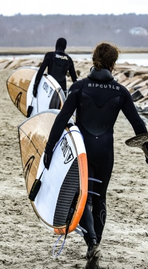 two persons in wet suits walking while carrying their surfing boards thumbnail