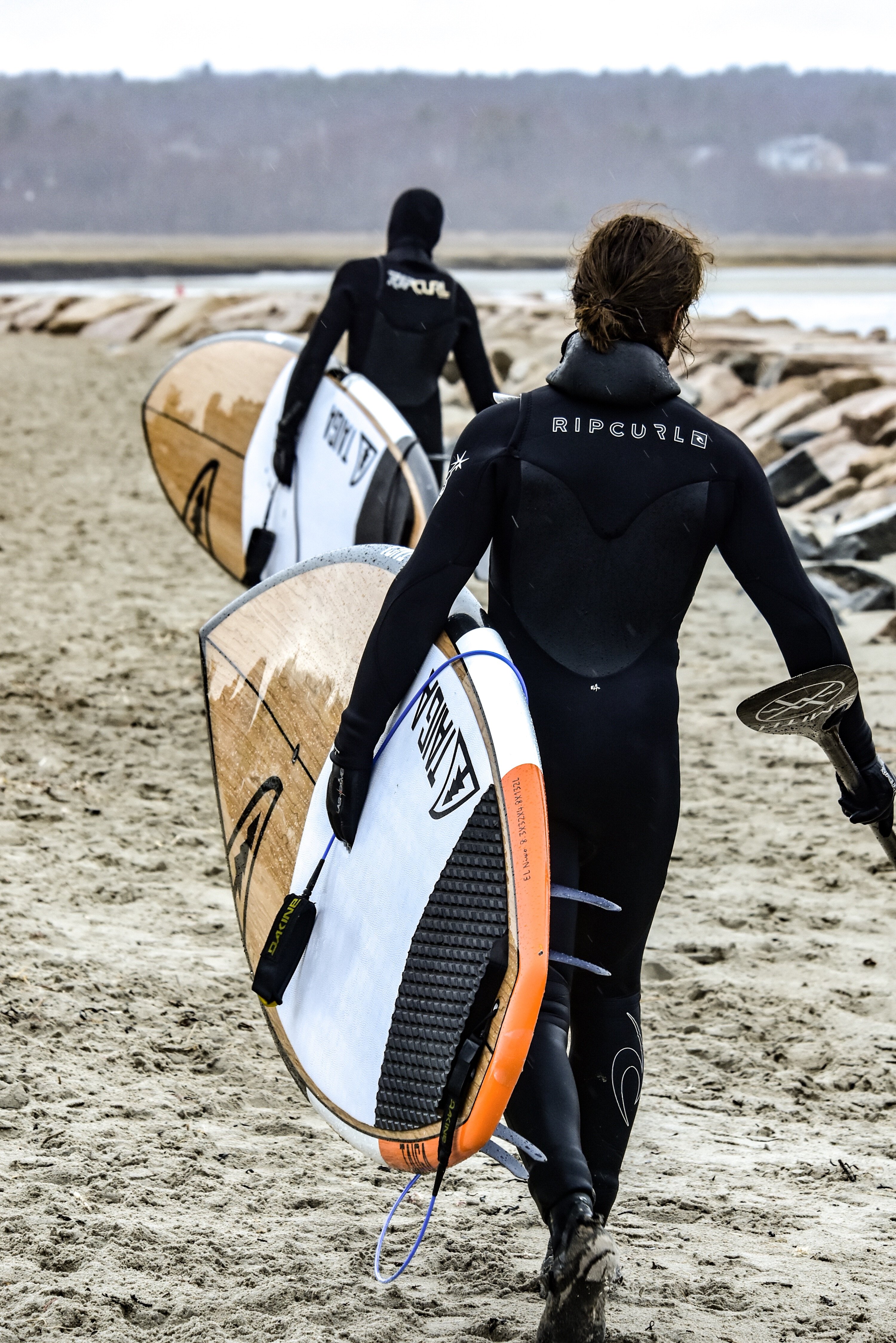 two persons in wet suits walking while carrying their surfing boards