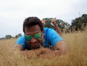 man wearing sunglasses and blue t-shirt lying on grass field thumbnail