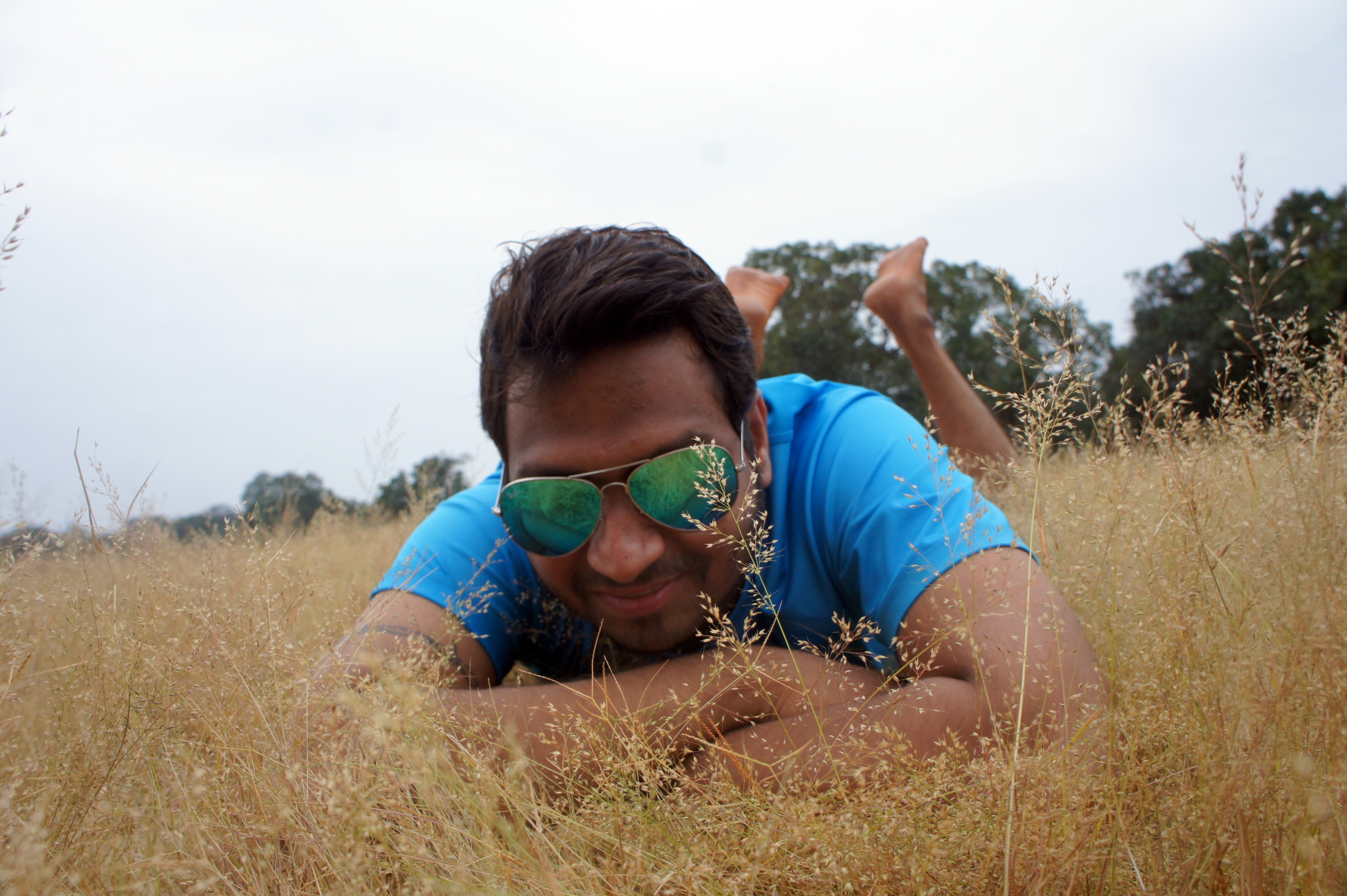 man wearing sunglasses and blue t-shirt lying on grass field