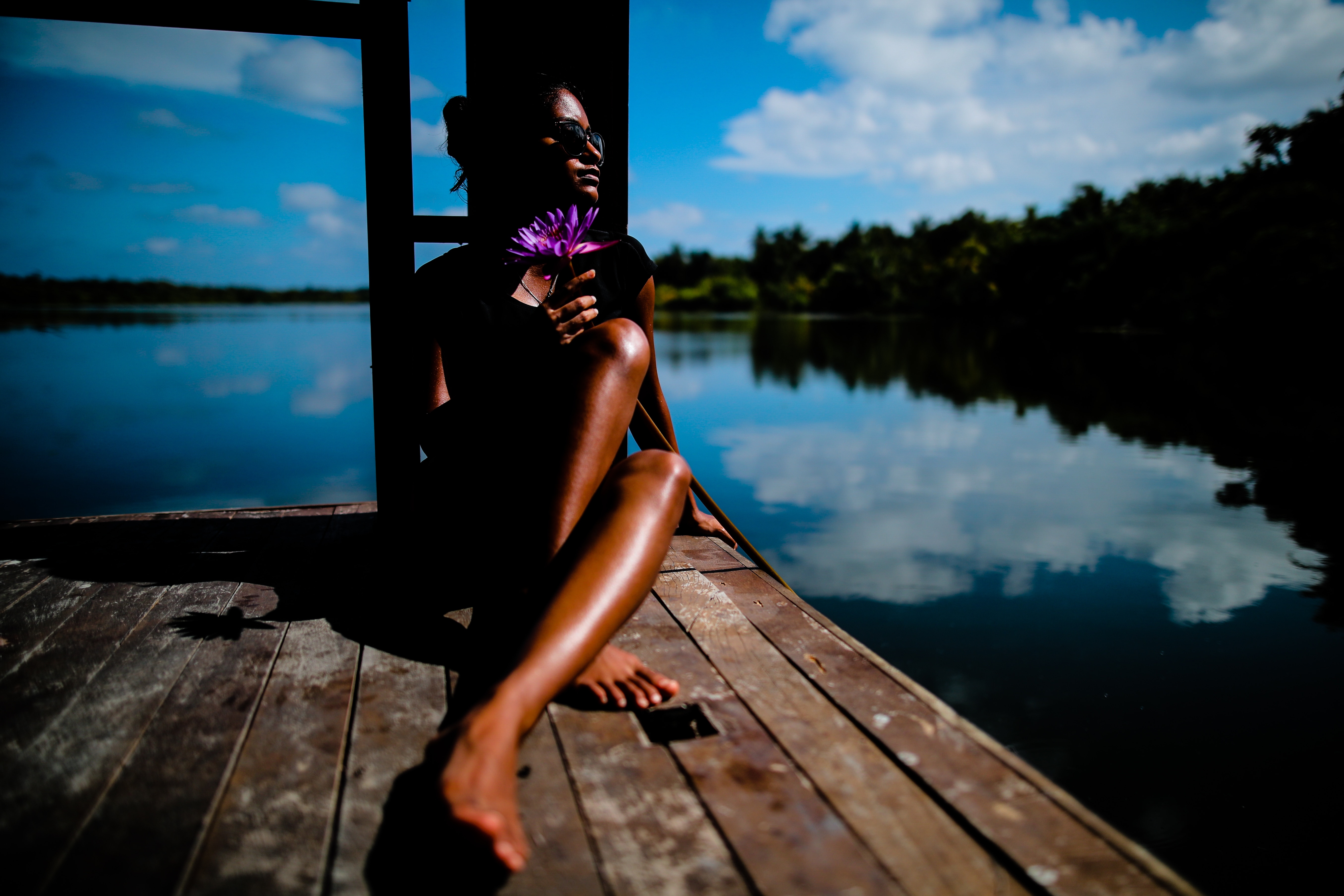 woman wearing sunglasses sitting on brown wooden parquet floor beside body of water during daytime