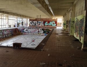 room with swimming pool with no water covered in graffiti thumbnail
