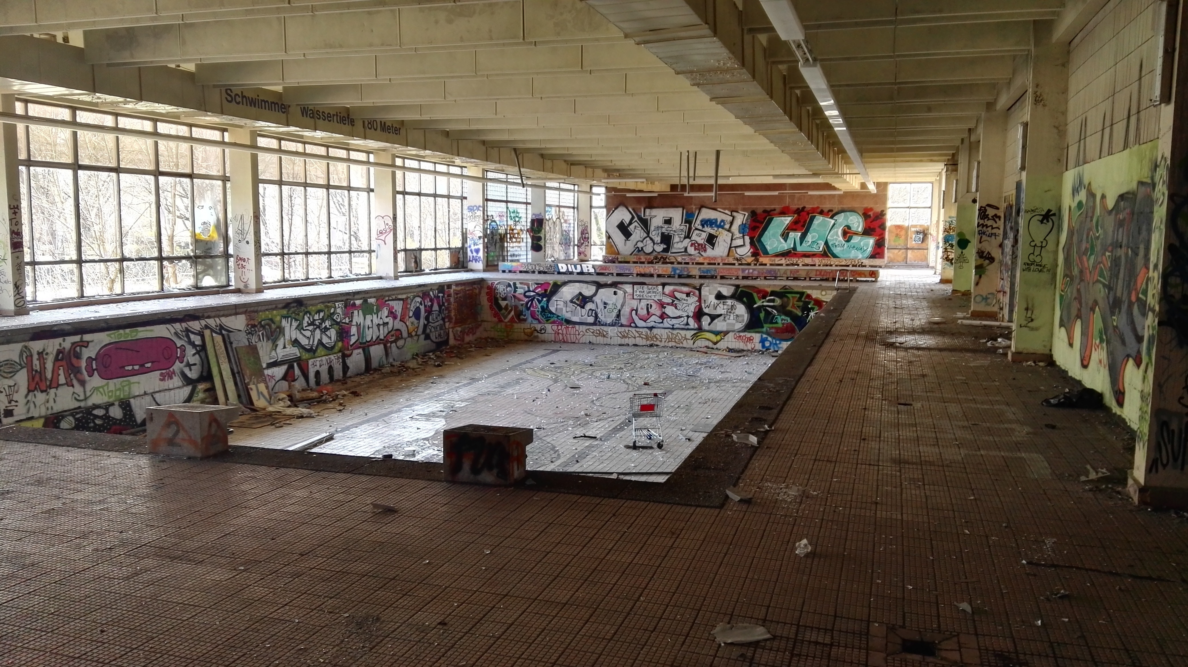 room with swimming pool with no water covered in graffiti