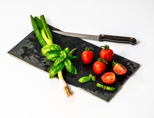 red tomatoes and and green leaf vegetable with black handled kitchen knife thumbnail