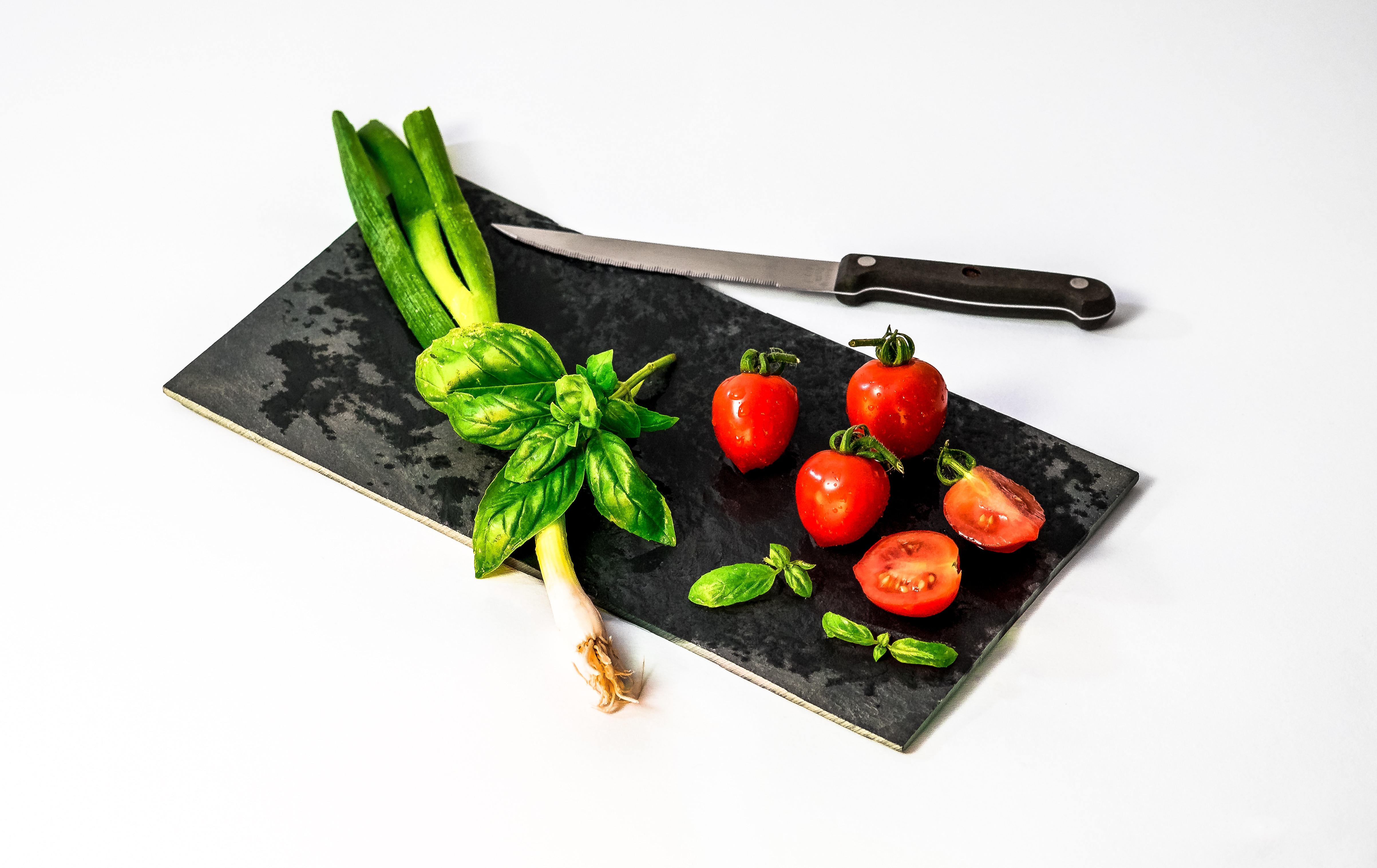 red tomatoes and and green leaf vegetable with black handled kitchen knife