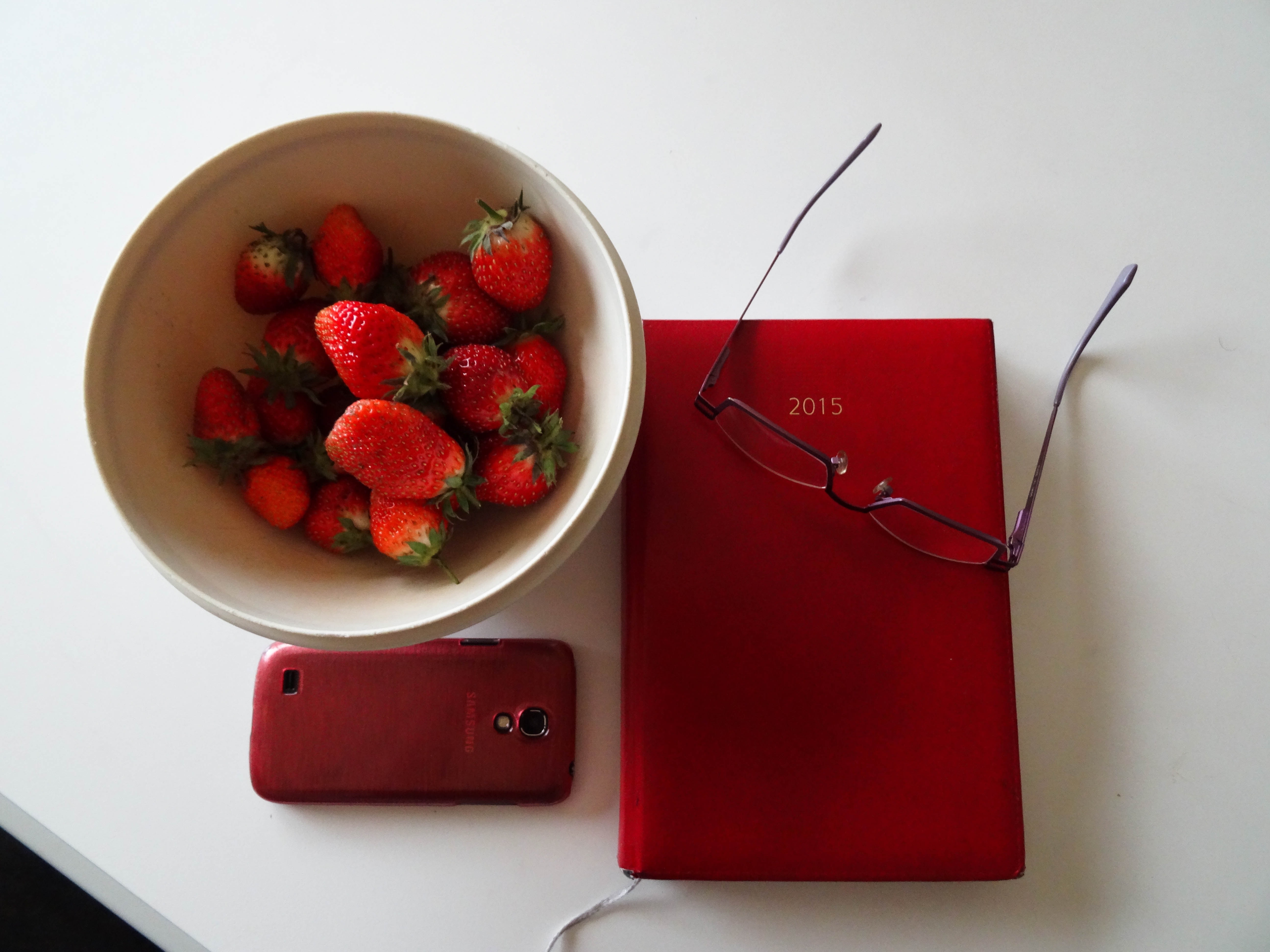 strawberry on ceramic bowl;red smartphone;red 2015 print book;red framed eyeglasses