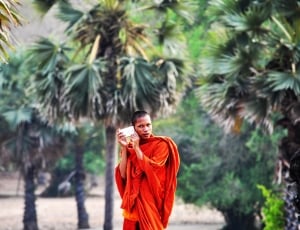 man wearing red traditional clothe standing near in a trees during daylight thumbnail