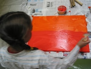 girl in stripes painting orange on canvas thumbnail