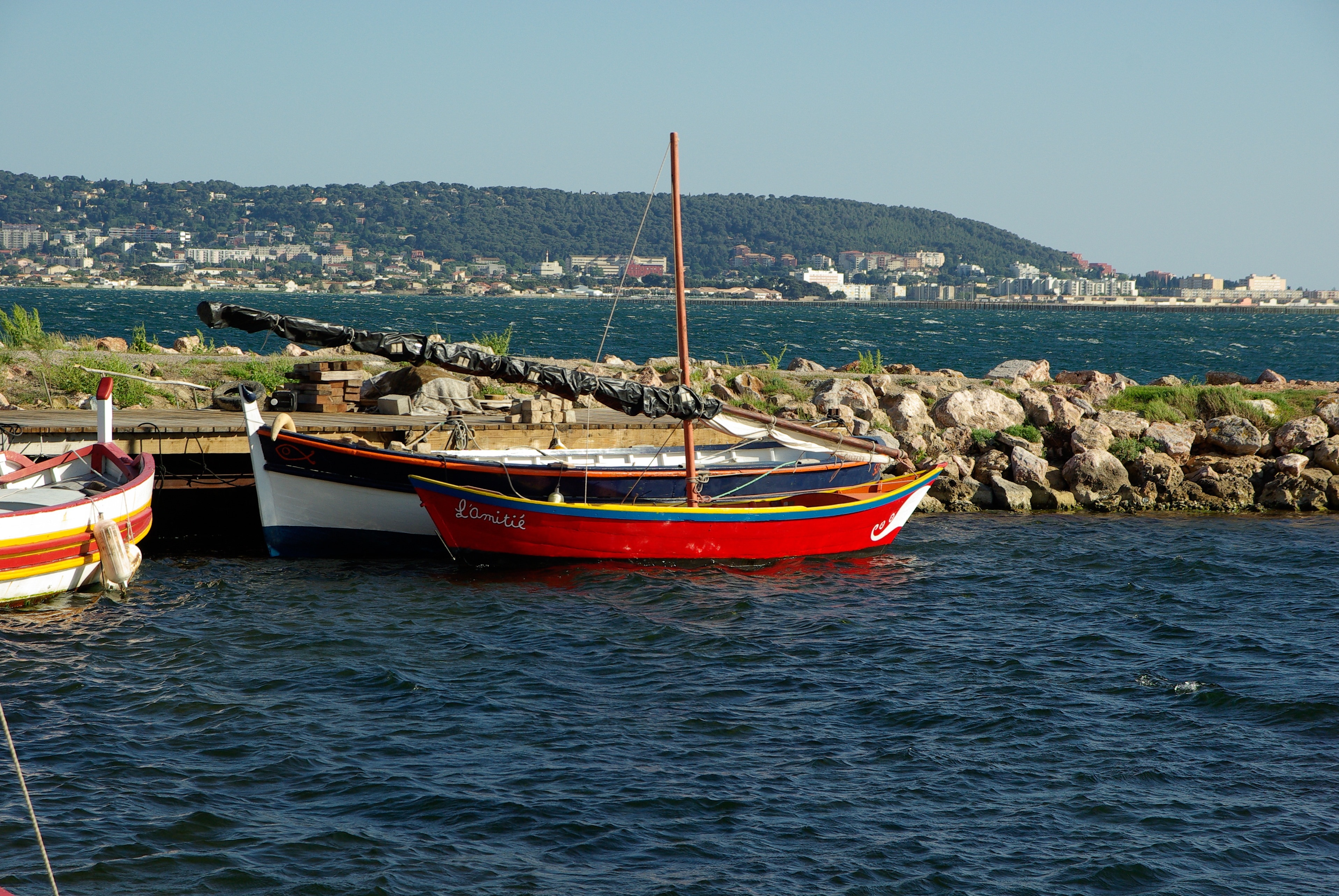 one red and one white boats on body of water along rocky shore under clear gray sky during daytime