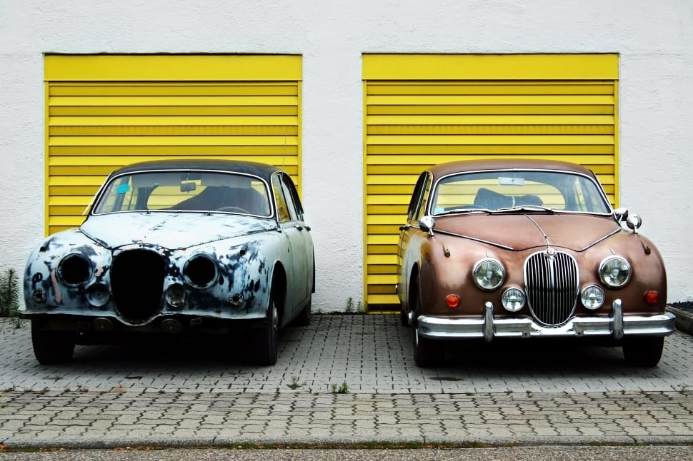 two vintage cars beside yellow shutter doors preview