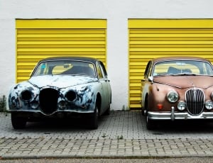 two vintage cars beside yellow shutter doors thumbnail