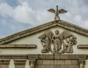 photo of three angel embossed on beige concrete building under white clouds thumbnail