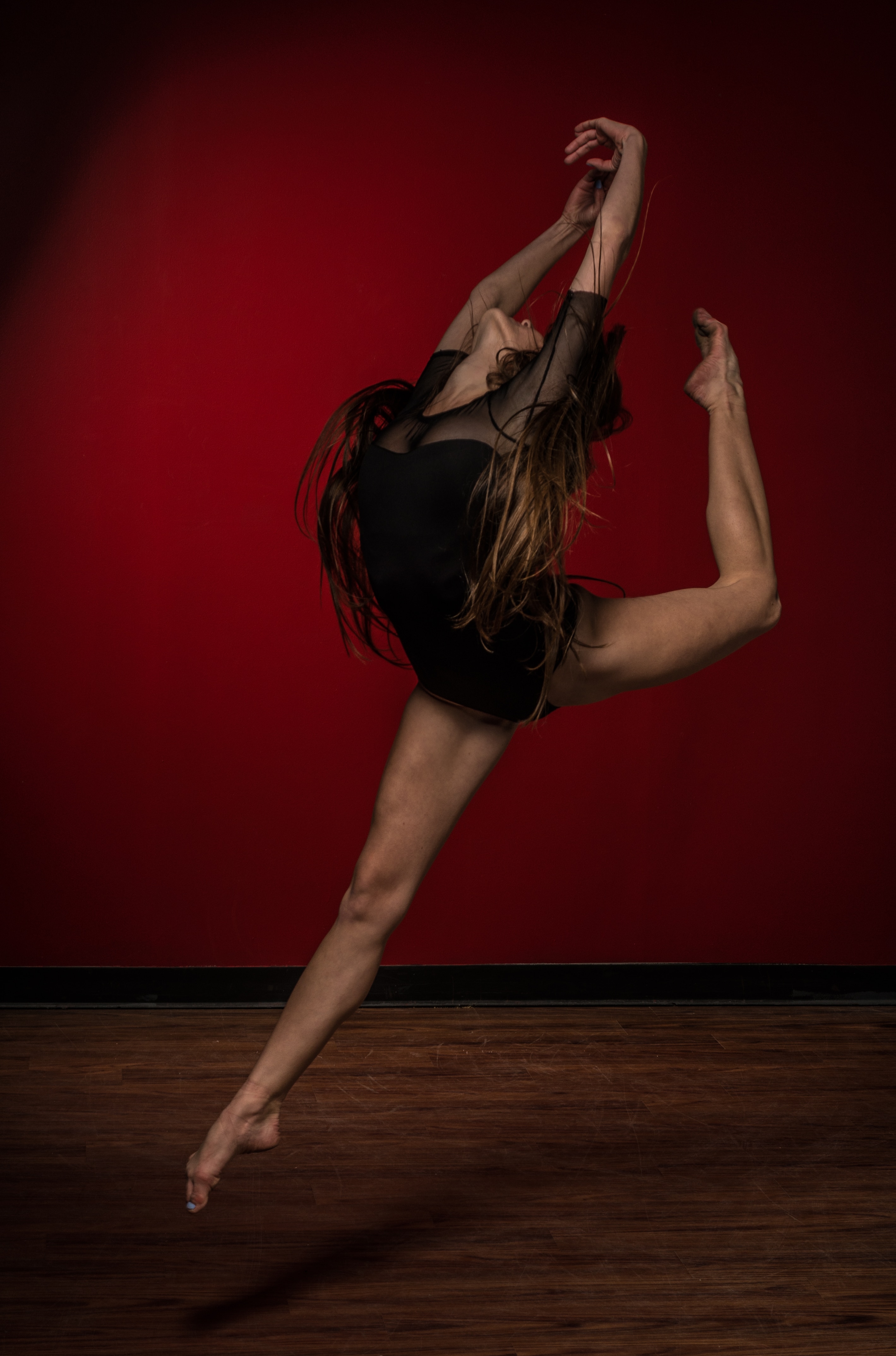 brunette haired woman in black leotard dancing ballet against red background