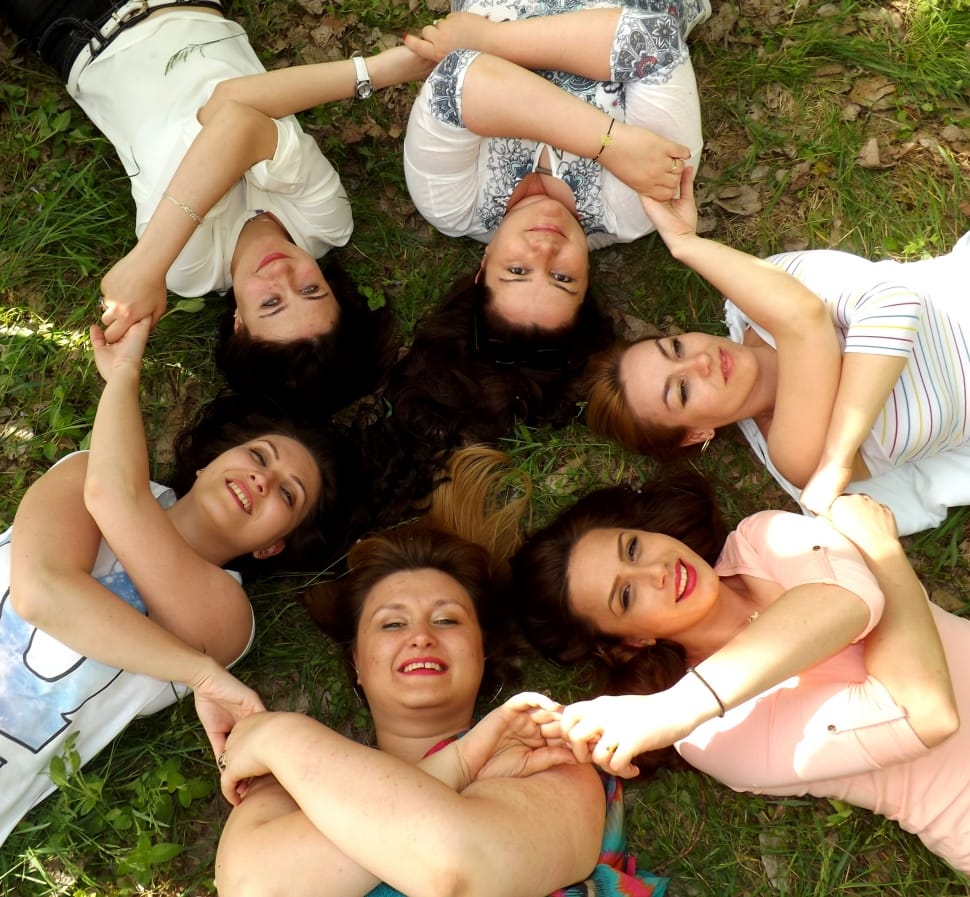 6 women lying on the ground forming circle while holding their hands and smiling preview