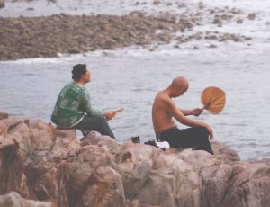 man and woman sitting on rock beside sea thumbnail