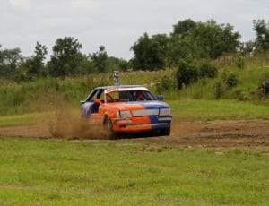 blue and orange racing car on dirt road during daytime thumbnail