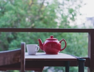 red ceramic teapot near white teacup on brown wooden table during daytime thumbnail