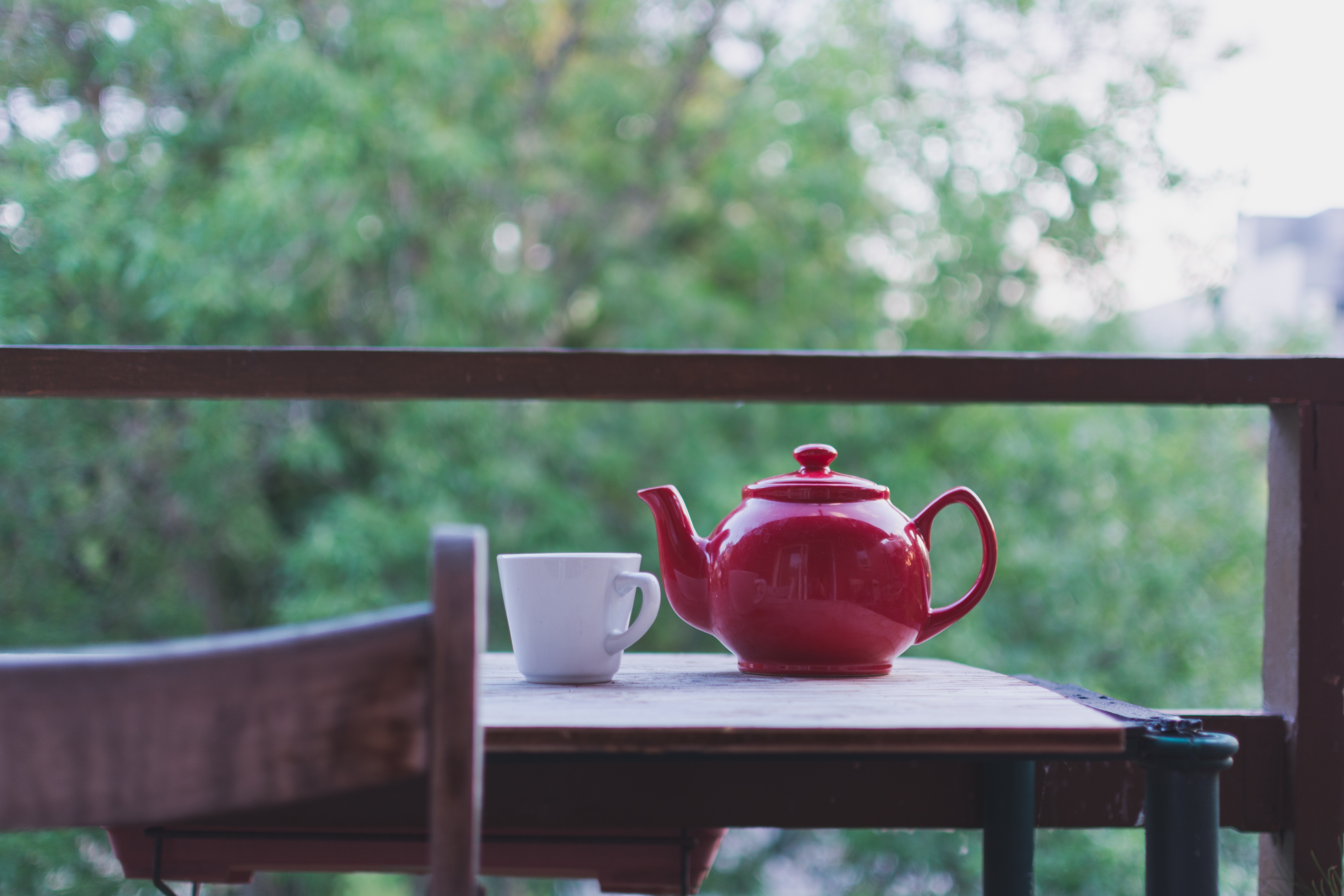 red ceramic teapot near white teacup on brown wooden table during daytime